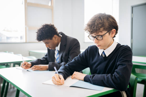 istock Focused male students writing in exam booklets 2162080697