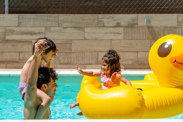 istock Father carrying son in pool, daughter on yellow duck float, all smiling and playing. 2162083191