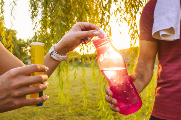 Unrecognizable Caucasian female and male athletes, pausing during their outdoor activity to refresh themselves with an effervescent tablet dissolved in a clear reusable water bottle