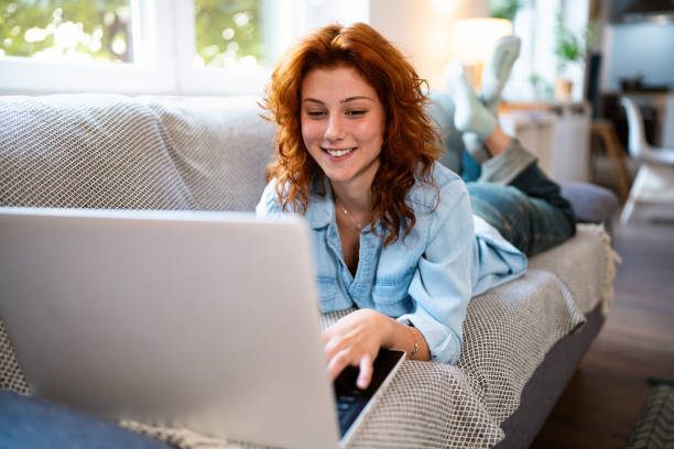 istock Young redhead Caucasian woman, working on laptop while relaxing on the sofa 2162085370