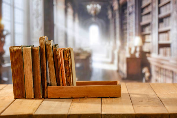 istock Old books on wooden table with space for prodcuts and blurred library with bright window light interior. 2162087647