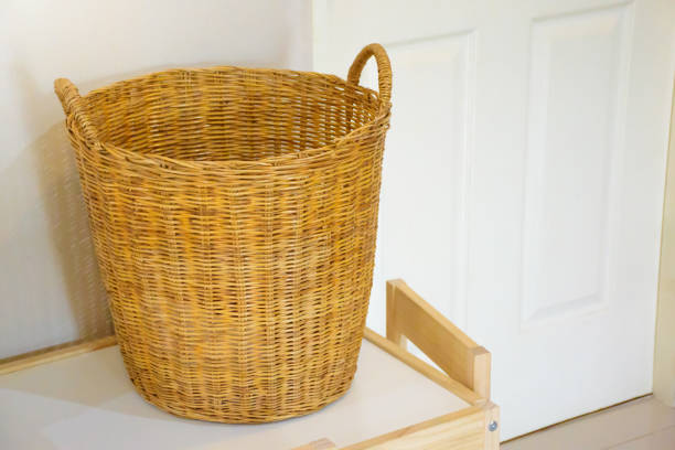 Large wicker laundry basket on white table against white door and wall background. Wicker basket laundry in bed room.