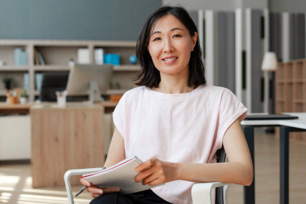 istock Attractive Asian businesswoman smiling while holding notebook in office 2162089656