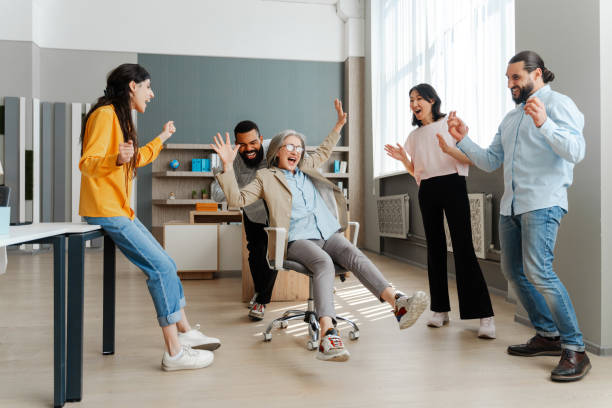istock Diverse, multinational team celebrating success pushing colleague on office chair 2162089699