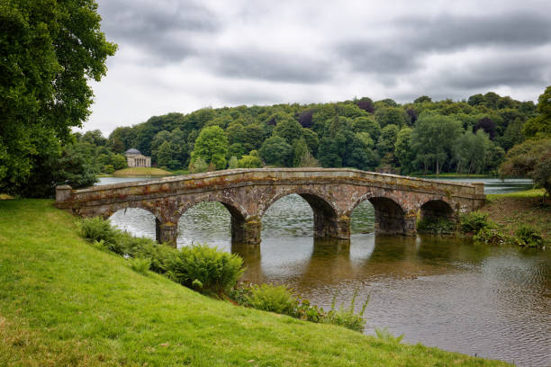 A scenic stone arch bridge over a tranquil river surrounded by lush greenery, capturing a serene natural setting.