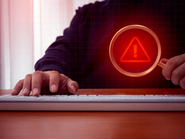istock Virus alert. Red triangle icon, System hacked error sign, malware, attention danger symbol warning showing in magnifying glass lens, holding by businessman hand who working with computer in dark room. 2162096667