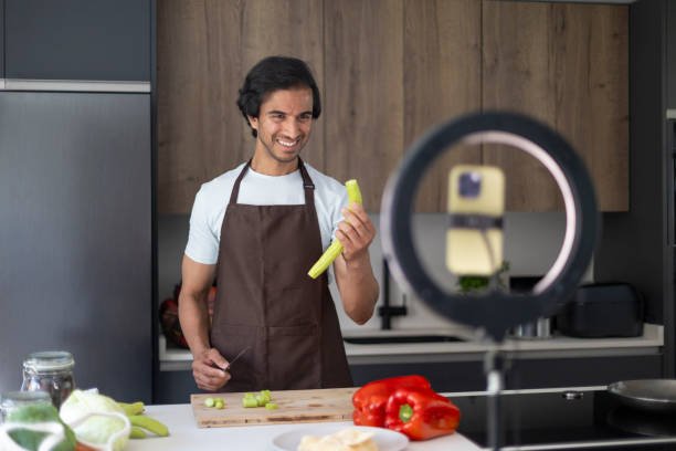 istock Smiling man in apron recording cooking video with fresh vegetables in kitchen. 2162097568