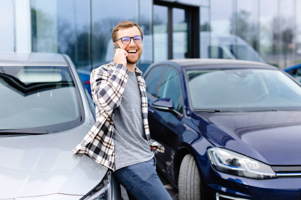 istock Handsome young man talking on the mobile phone and smiling while leaning at his car 2162099882