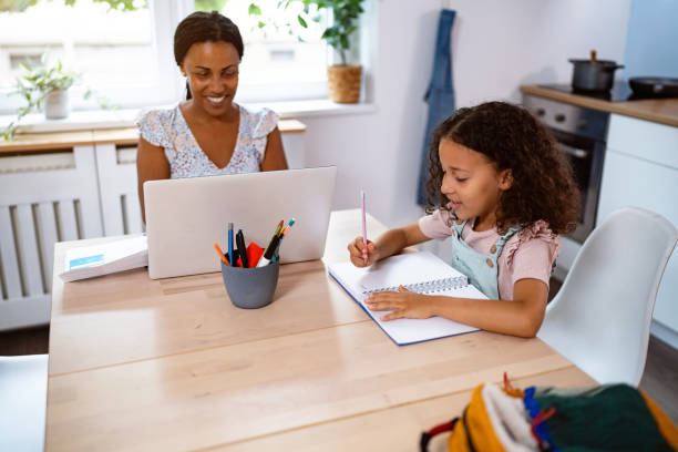 istock Schoolgirl Black ethnicity doing her homework, while her mother working on laptop 2162100124