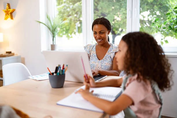 istock Daughter Black ethnicity doing her homework, while her mother working on laptop from home 2162100125