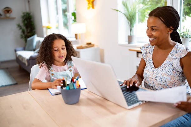 istock Daughter Black ethnicity doing her homework, while her mother working on laptop from home 2162100129