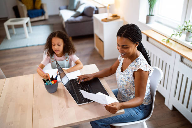 Woman Black ethnicity working on laptop while her daughter doing her homework