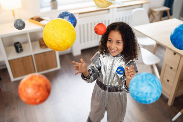 istock Curious multiracial girl in a space suit playing with handmade planets 2162100361
