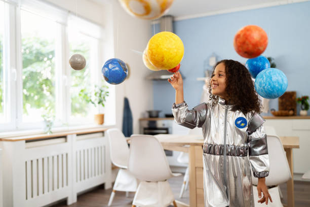 istock Curious multiracial girl in a space suit playing with handmade planets 2162100448