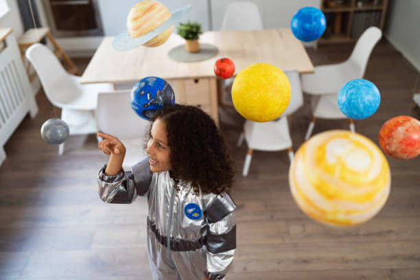 istock Curious multiracial girl in a space suit playing with handmade planets 2162100528