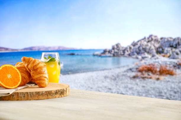 Summer continental breakfast on a beach. Croissants, jam and fruit on a wooden table. Summer table background for montage product display. Copy space for food and drink and products. Greece holiday resort.