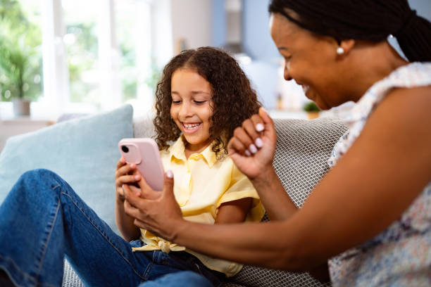 istock Multiracial girl with her mother Black ethnicity, using a mobile phone, while sitting on a sofa 2162101199