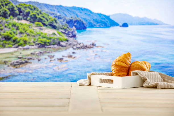 Summer continental breakfast on a beach. Croissants, jam and fruit on a wooden table. Summer table background for montage product display. Copy space for food and drink and products. Greece holiday resort.