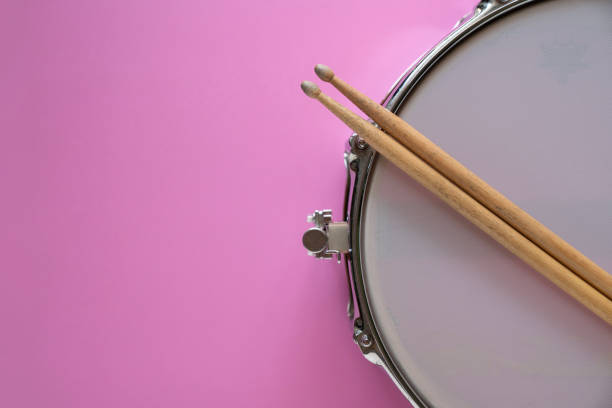 Drum stick and drum on pink table background, top view, music concept