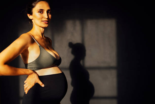 istock Pregnant woman against a gray texture wall with shadow silhouette 2162112421