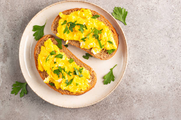 istock Scrambled eggs with green herbs on wheat-rye crispy toast. 2162112530