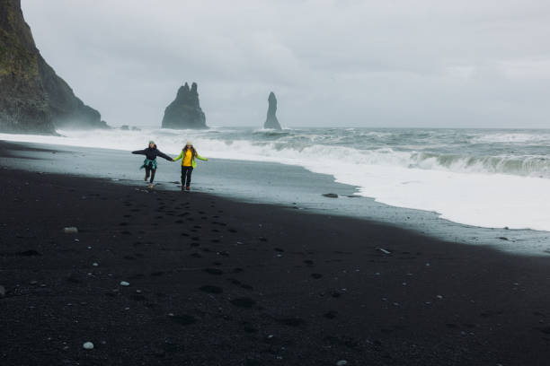 istock Two Happy Travellers Running at Dramatic Black Sand Beach With Ocean Views in Iceland 2162118848
