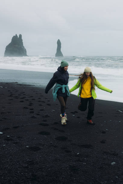 istock Two Happy Travellers Running at Dramatic Black Sand Beach With Ocean Views 2162118961