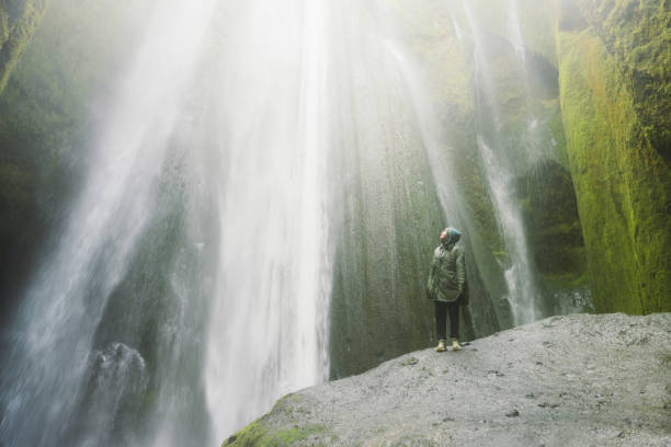 istock Woman Contemplating Dramatic Waterfall Hidden in Cave in Iceland 2162119026