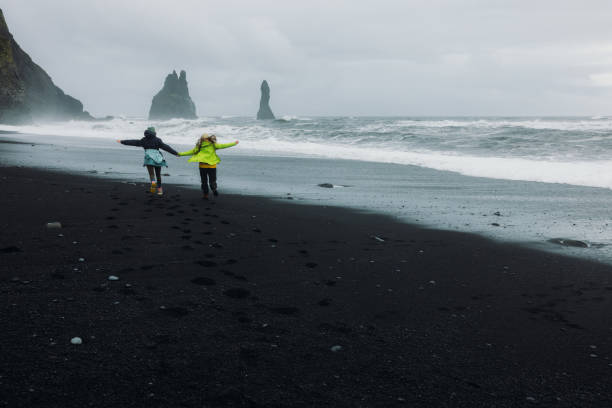 istock Two Happy Travellers Running at Dramatic Black Sand Beach With Ocean Views 2162119030