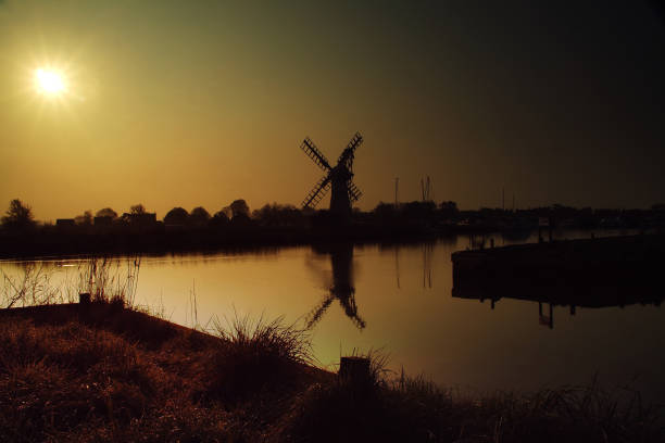the warmth of the sun lights the water and sky whilst leaving Thurne windmill in a misty morning in silhouette