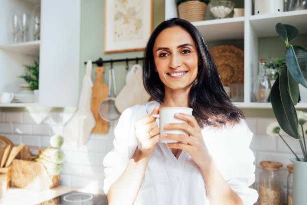 istock A charming young woman stands in a sunlit kitchen and holds a white mug 2162120670