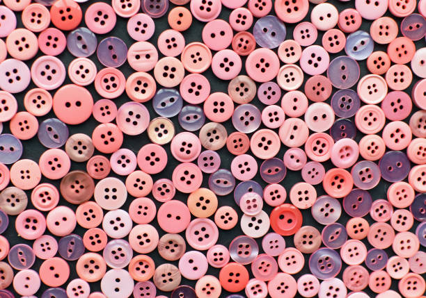 Large collection or arrangement of multi coloured pastel pink sewing buttons. Navy blue black background. Full or crowded space. Needlecraft, tailoring or hobby. Monochrome retro abstract pattern and texture. Flat lay from above