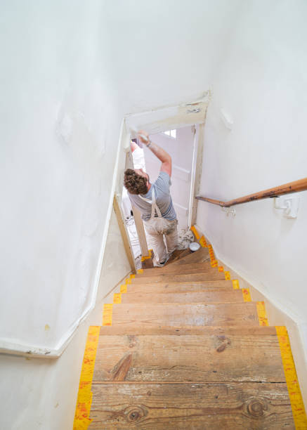 Young professional painter and decorator overcoming the disability of having one hand painting an old staircase door and frame.