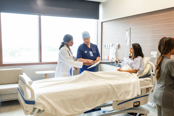 Doctors confer while patient listens and nurse takes notes The mature adult female doctor and mature adult male surgeon confer while the young adult female patient on the gurney listens and the unrecognizable female nurse in the foreground takes notes. doctor and hospital stock pictures, royalty-free photos & images