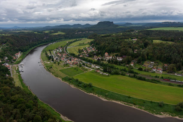 A river runs through a town with houses and trees. The sky is cloudy and the water is brown