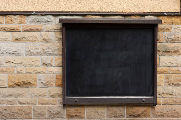 A black inscription board hangs on a stone wall. Black board on an old stone wall.