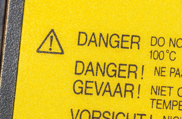 Bright yellow danger hazard label sticker symbol with a exclamation mark in a triangle symbol on a lithium-ion laptop computer device li-ion battery, object detail, closeup, nobody, multiple languages
