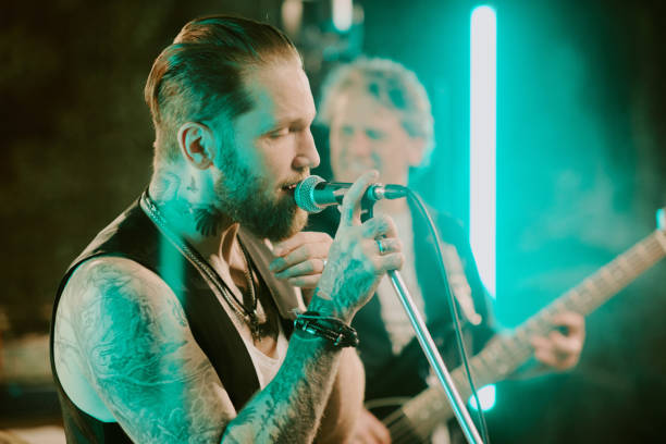 Medium closeup of Caucasian vocalist with beard on face and tattoos on body singing rock song on stage, copy space