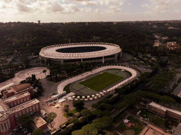 A breathtaking aerial view of Rome's Stadio Olimpico at sunset, captured in all its majestic glory. This iconic stadium, nestled amidst the lush greenery of the eternal city, perfectly balances modernity and history, offering a unique emotional experience to all who behold it.