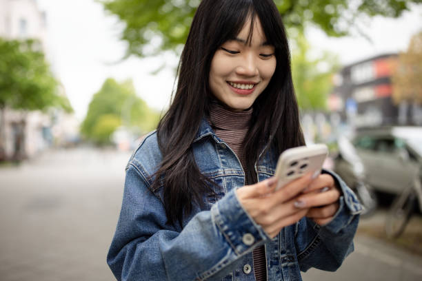 istock Smiling young asian woman using mobile phone walking outside 2162141977