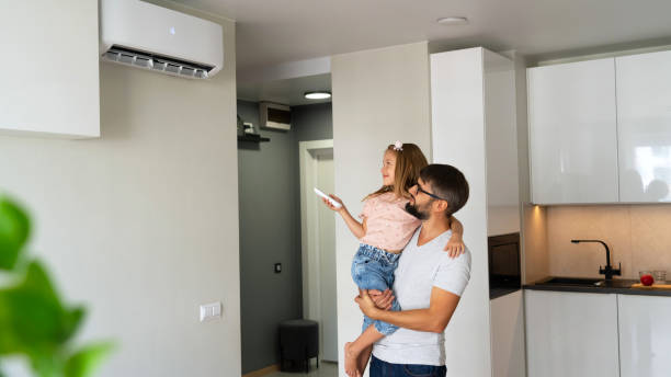 Father with daughter turn on air conditioner using remote control. Father with little daughter on hands turn on air conditioner using remote control. Happy family adjust comfortable temperature of cooler system air conditioner family stock pictures, royalty-free photos & images