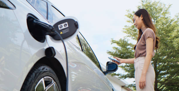 Asian woman charging electricity on modern EV car, use mobile phone app to lock. Electric vehicle technology, sustainable clean energy, zero waste emission, environmental conservation lifestyle mujer asiática cargando electricidad en un automóvil ev moderno, use la aplicación de teléfono móvil para bloquear. tecnología de vehículos eléctricos, energía limpia sostenible, cero emisiones de residuos, estilo de vida de conservación del medi