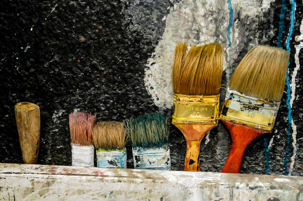 A row of paintbrushes are lined up on a wall. The brushes are of different sizes and colors, and they appear to be old and worn. Concept of nostalgia and the passage of time