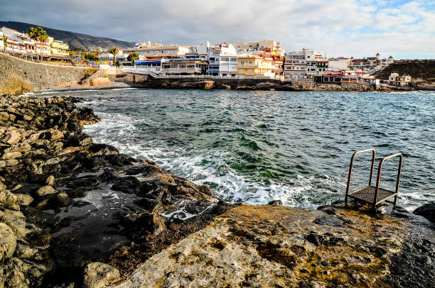 A rocky shoreline with a small pool and a ladder. The water is calm and the sky is cloudy