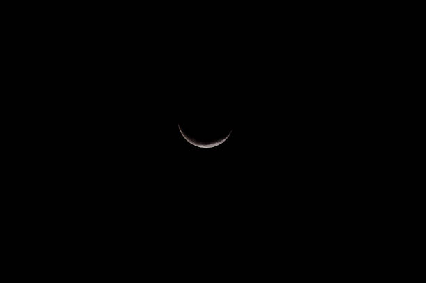 A black and white photo of a crescent moon. The moon is the main focus of the image, and it is the only object in the frame. The photo has a moody and mysterious feel to it