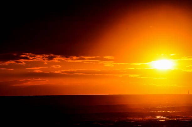 The sun is setting over the ocean, casting a warm glow over the water. The sky is filled with clouds, creating a moody atmosphere