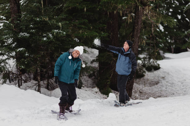 istock Man throws snowball at partner while snowshoeing together 2162163059