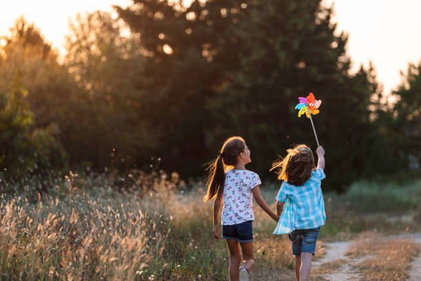 Two kids playful with pinwheel on rural path at sunset.