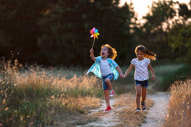 A vibrant image of children running with a pinwheel along a natural path, encapsulating carefree joy, energy, and togetherness amidst the serene outdoor setting at dusk.
