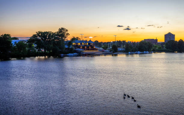 Boston, Massachusetts, USA - July 11, 2024: Sunset over the Charles River and Harvard University's Newell Boathouse. The Newell Boathouse, named for a popular Harvard athlete killed just a few years after graduation, is the primary boathouse used by Harvard University's varsity men's rowing teams. Built in 1900 on the south side of the Charles River. it was Harvard's first permanent boathouse.